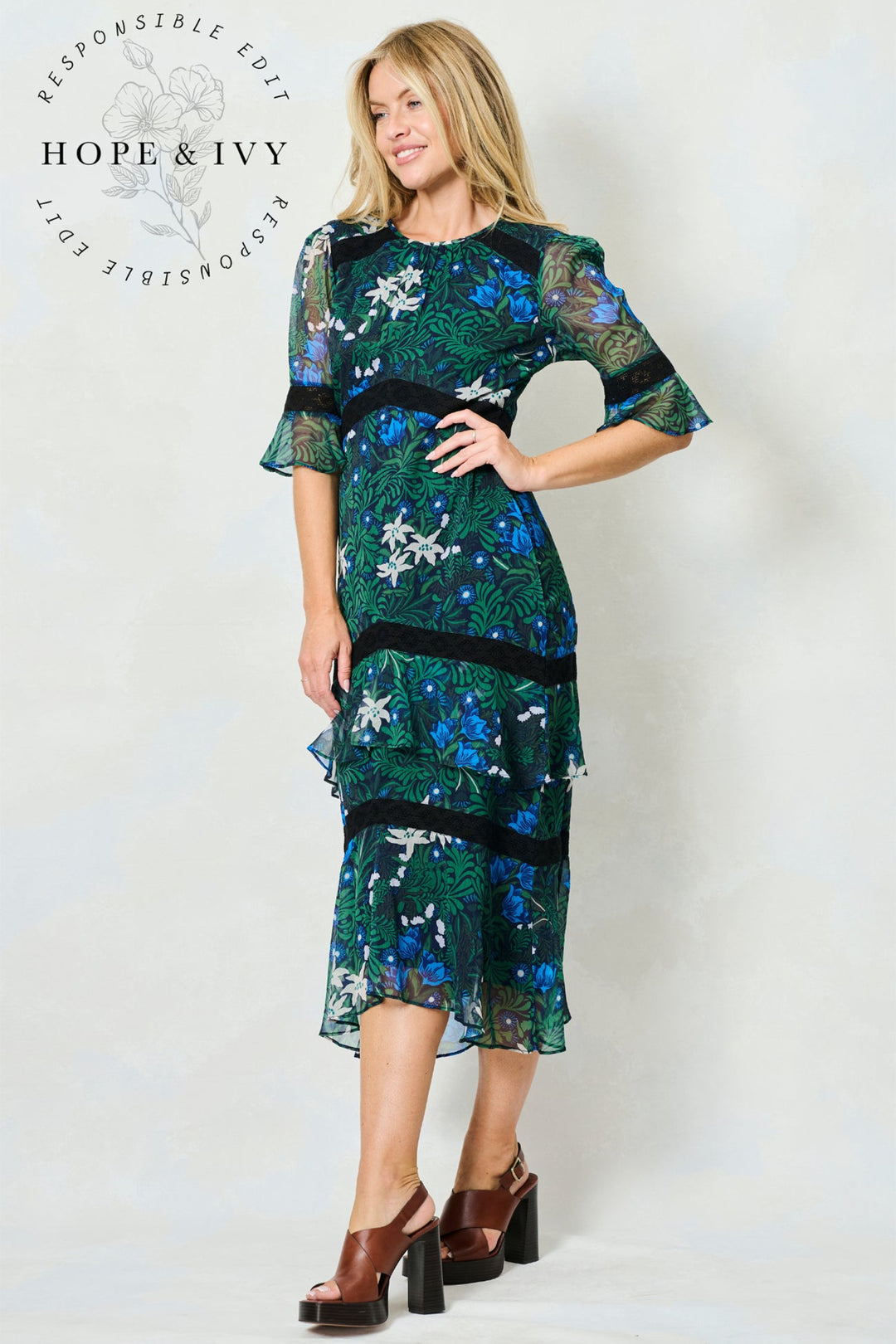 Woman wearing a green floral dress with 'Hope & Ivy' branding on a white background