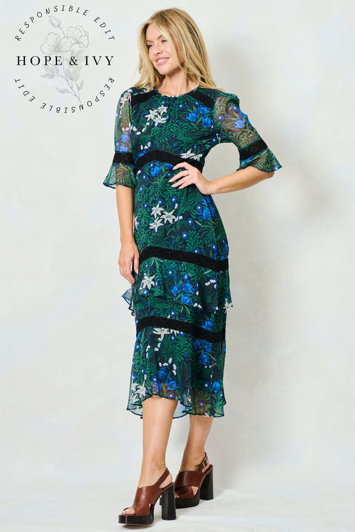 Woman wearing a green floral dress with 'Hope & Ivy' branding on a white background