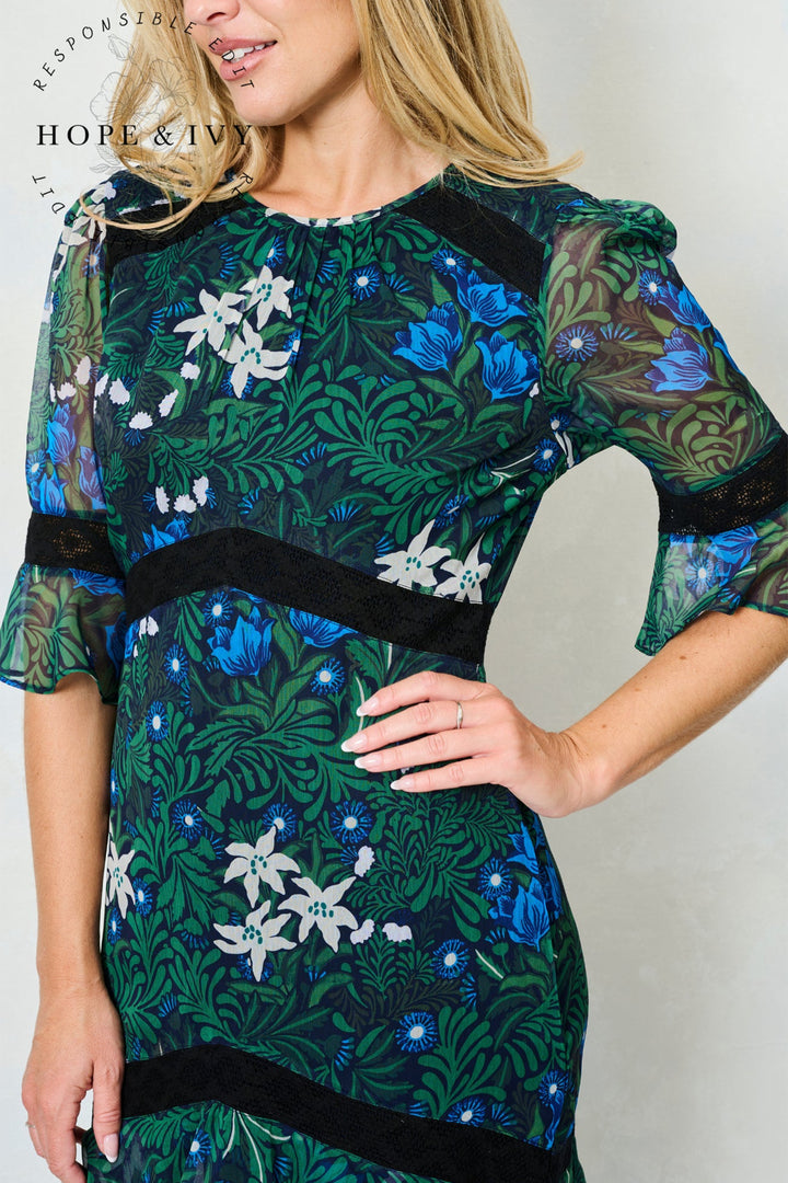 Woman wearing a floral dress with a visible brand logo on a plain background