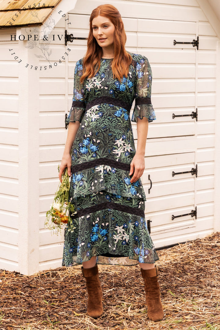 Woman in a floral dress standing in front of a white wooden door with 'Hope & Ivy' branding.