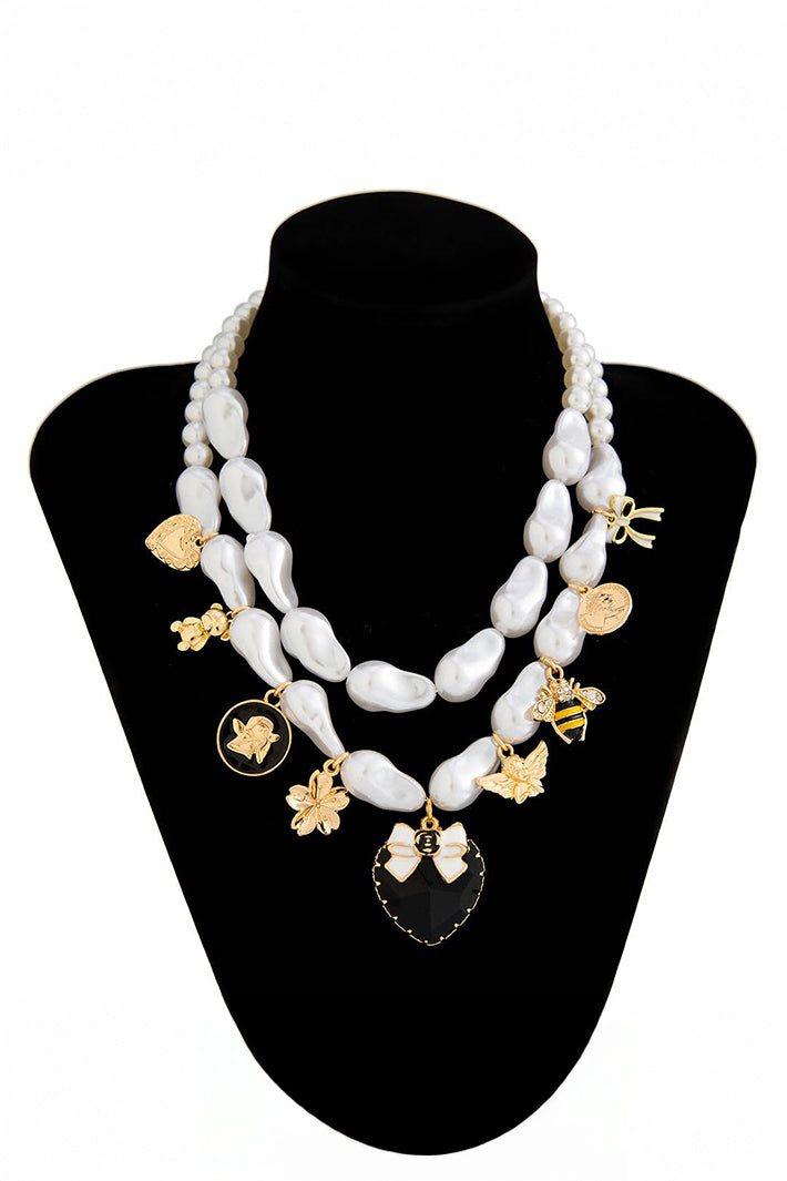 Pearl necklace with gold and black charms on a black stand
