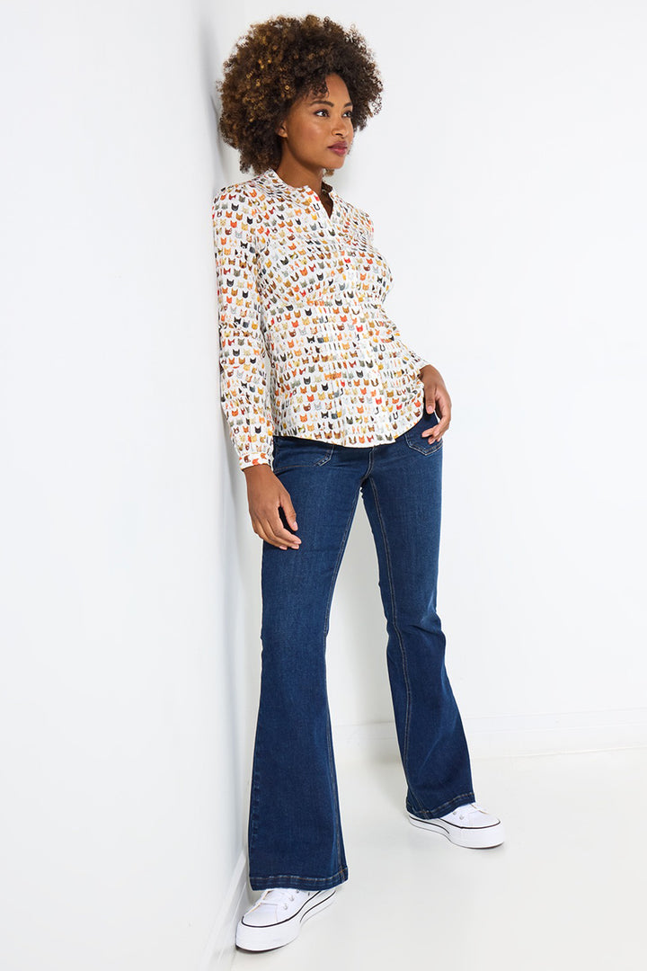 Woman wearing a patterned blouse and blue jeans against a white background