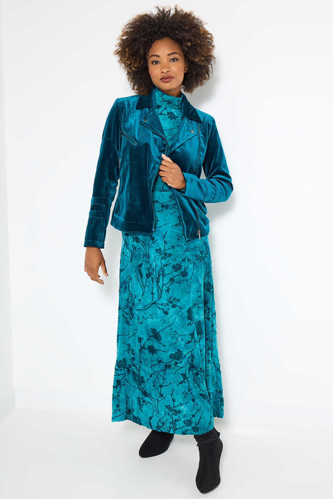 Woman wearing a teal velvet jacket and matching dress on a white background
