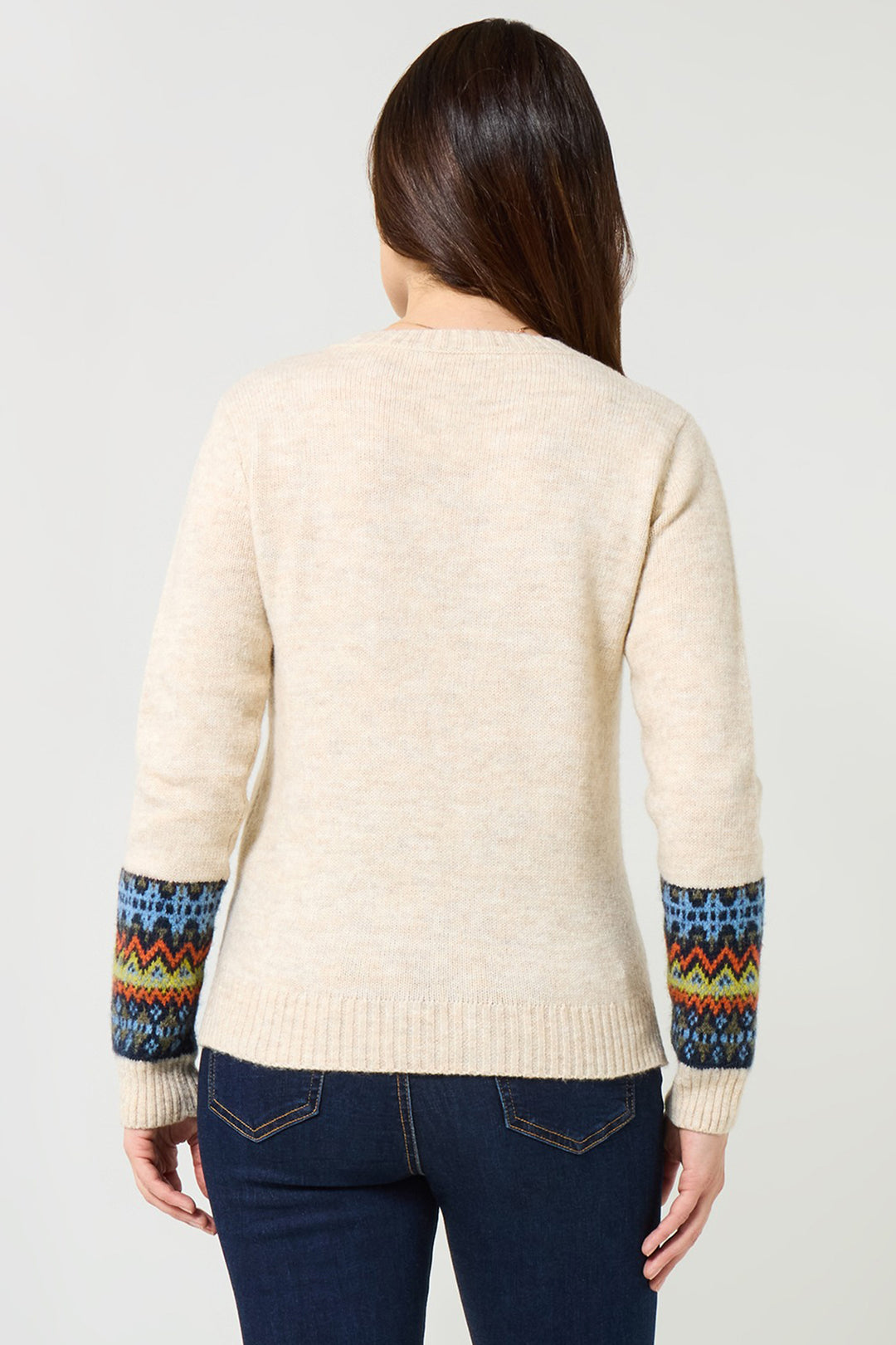 Woman wearing a cream sweater with colorful sleeve patterns on a plain background