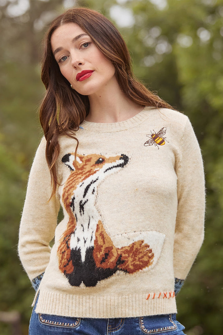 Woman wearing a cream sweater with a fox design outdoors