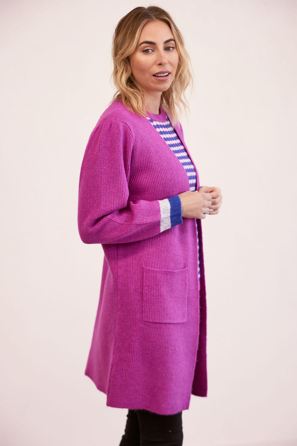 Woman wearing a bright pink cardigan over a striped shirt on a light pink background