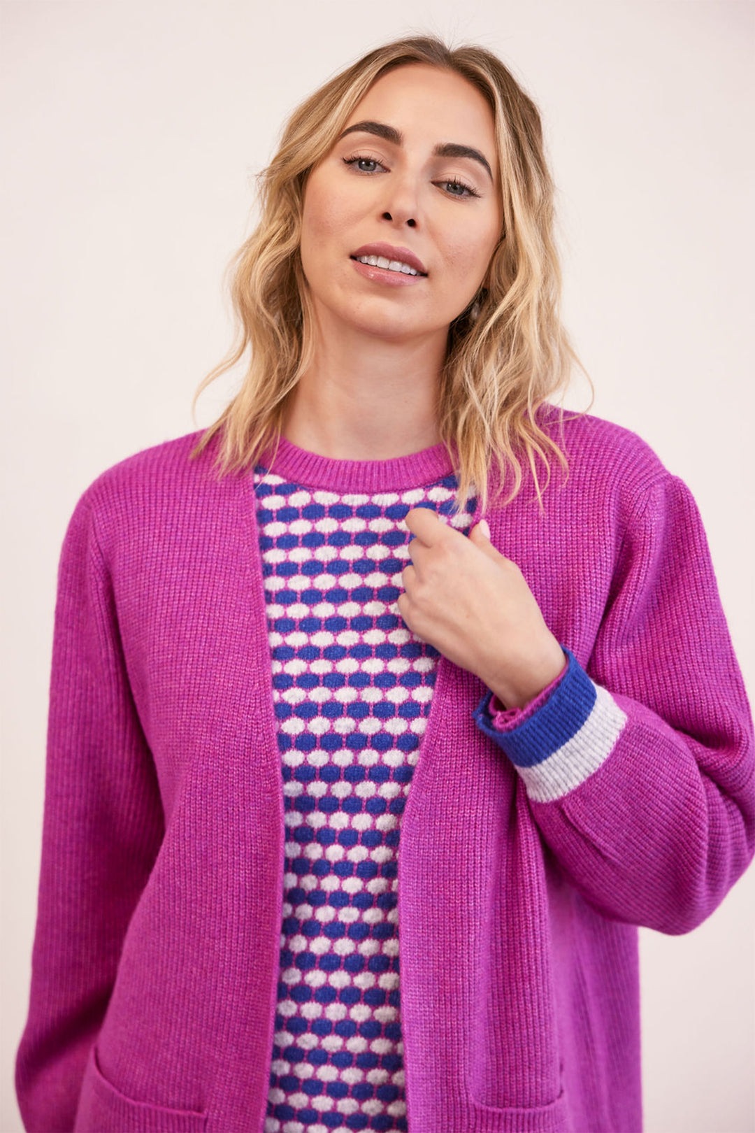 Woman wearing a bright pink cardigan over a patterned shirt on a plain background