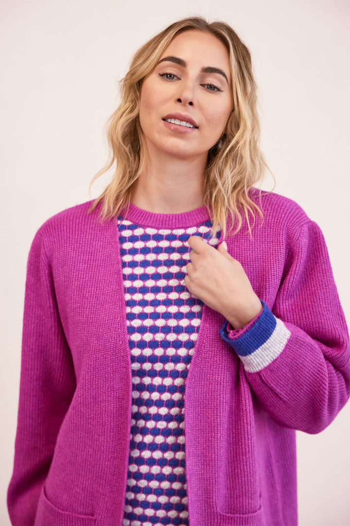 Woman wearing a bright pink cardigan over a patterned shirt on a plain background