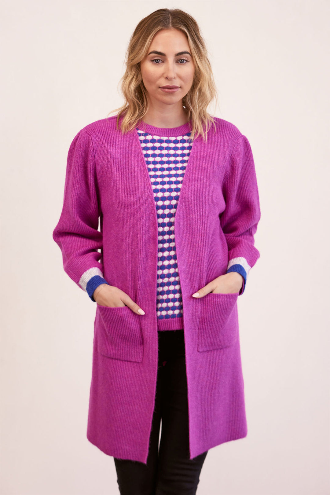 Woman wearing a long purple cardigan over a patterned top on a plain background
