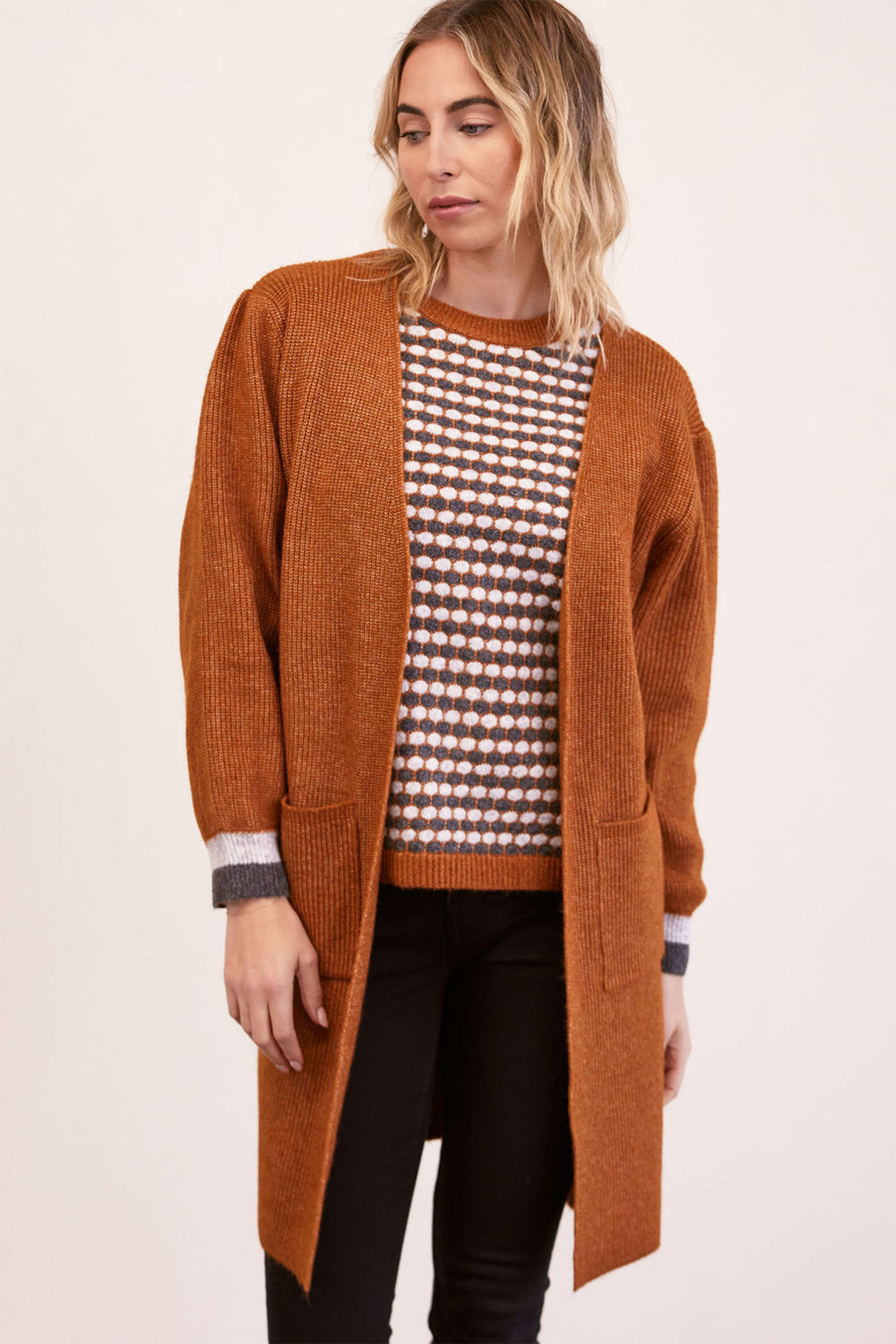 Woman wearing a long brown cardigan over a patterned shirt on a beige background