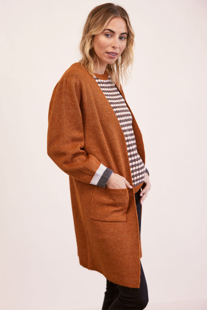 Woman wearing a long brown cardigan over a patterned shirt on a beige background