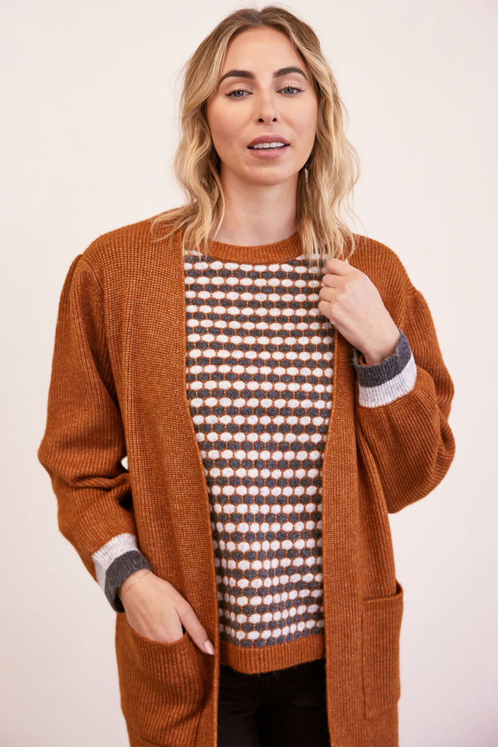 Woman wearing a brown cardigan over a patterned shirt on a plain background