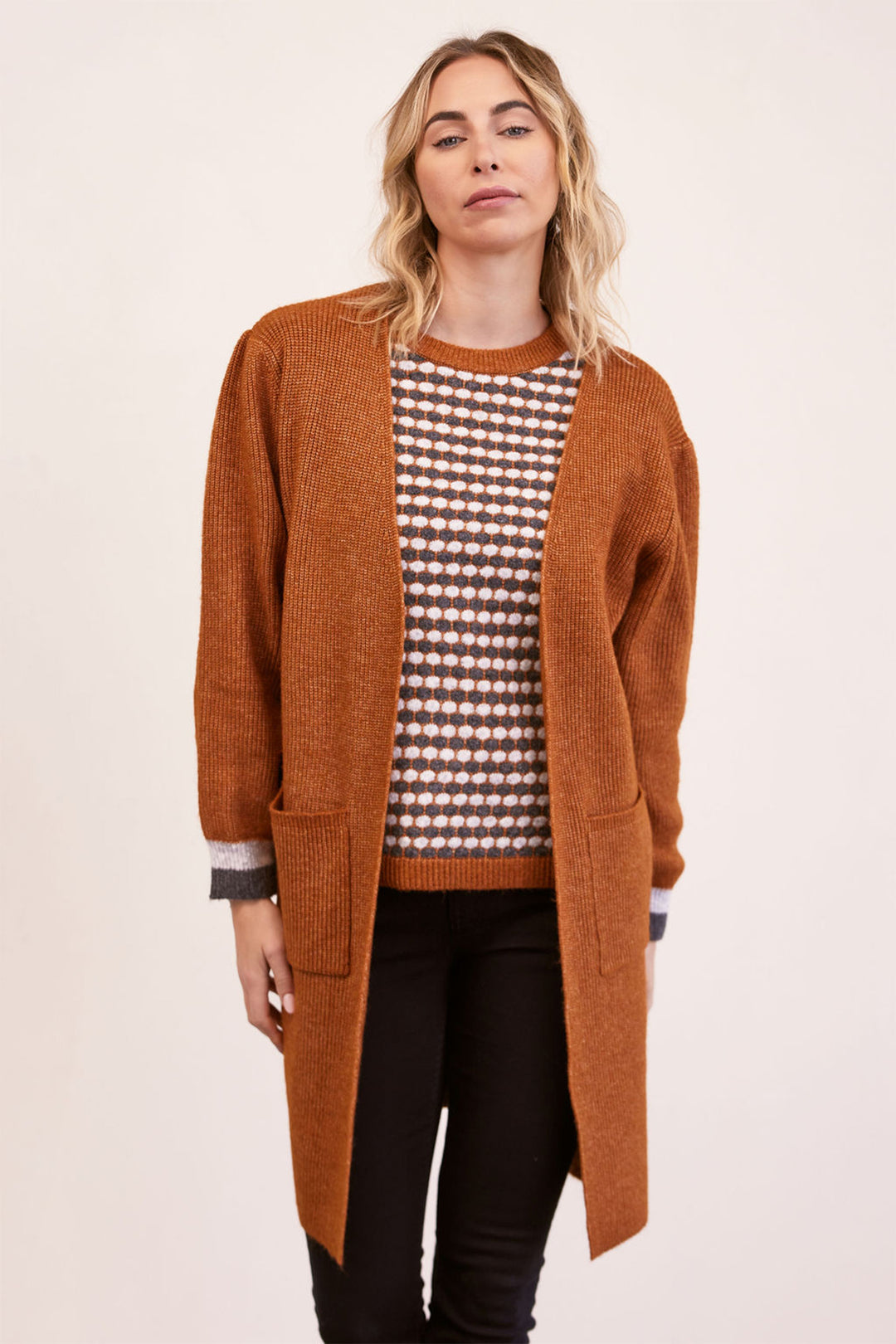 Woman wearing a long brown cardigan over a patterned shirt on a white background