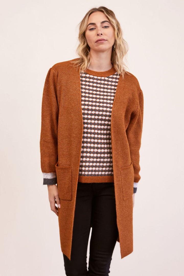 Woman wearing a long brown cardigan over a patterned shirt on a white background