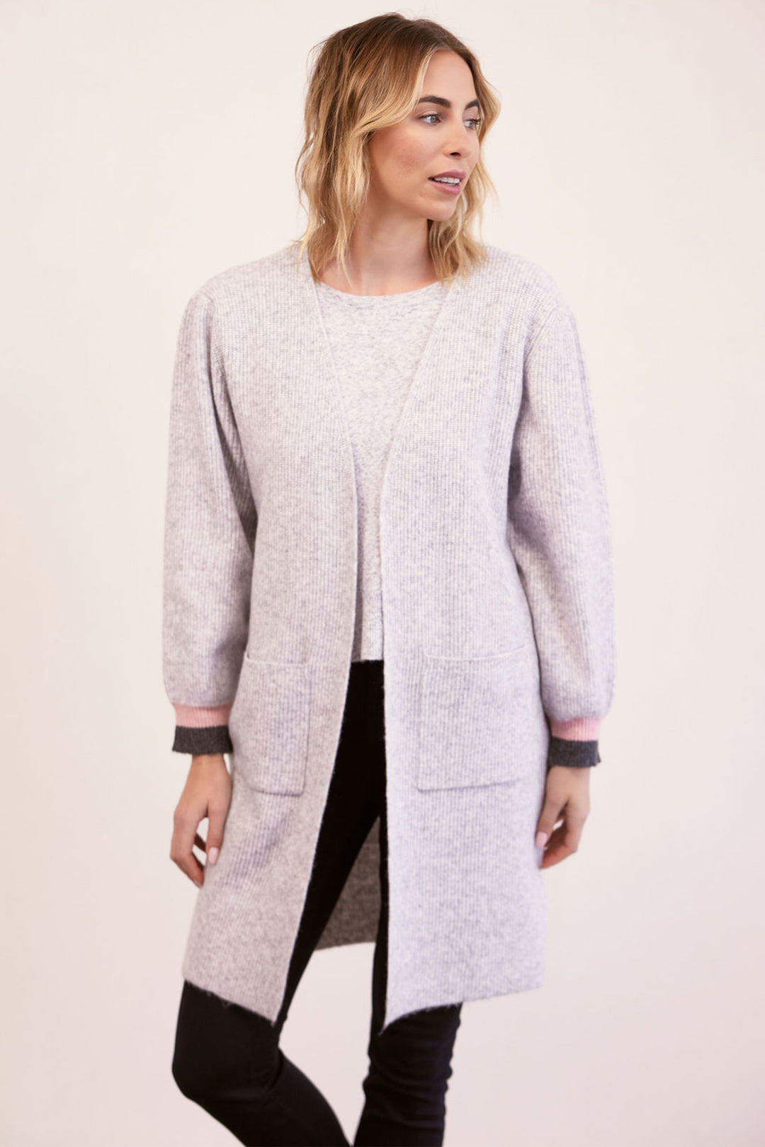 Woman wearing a long light gray cardigan on a plain background