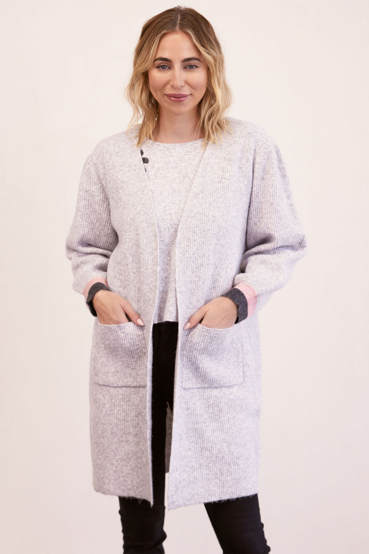 Woman wearing a light gray cardigan over a white top on a plain background