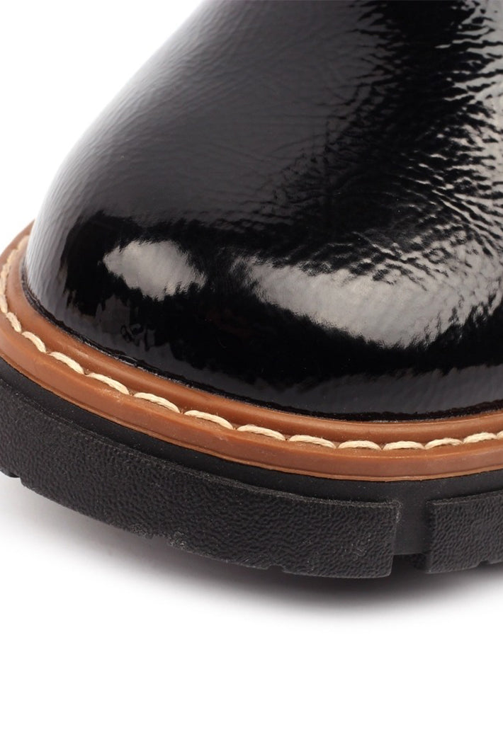 Close-up of a black patent leather shoe with brown trim on a white background