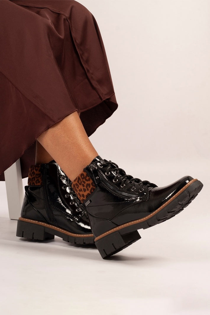 Person wearing black patent leather boots with brown accents on a white background