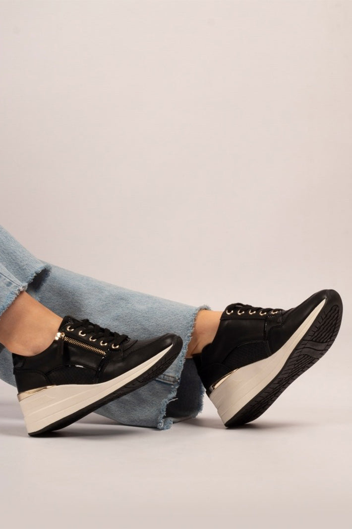 Black sneakers with white soles worn with light blue jeans on a neutral background