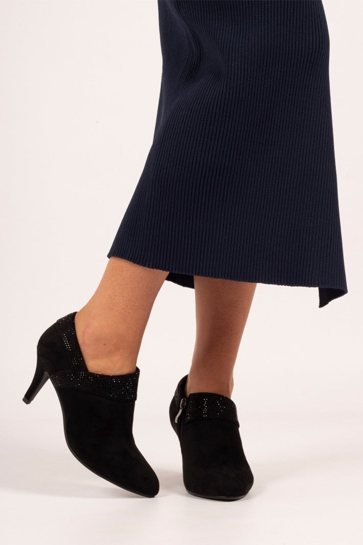 Black high-heeled shoes with decorative elements worn with a navy skirt on a white background