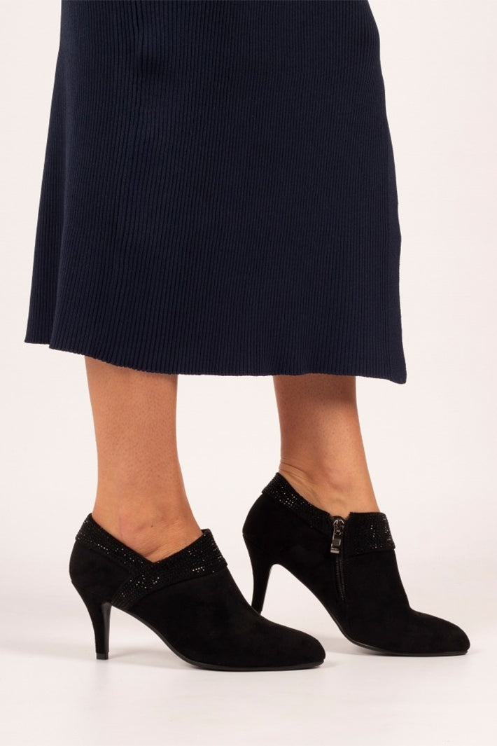 Black high-heeled shoes worn with a black skirt on a white background