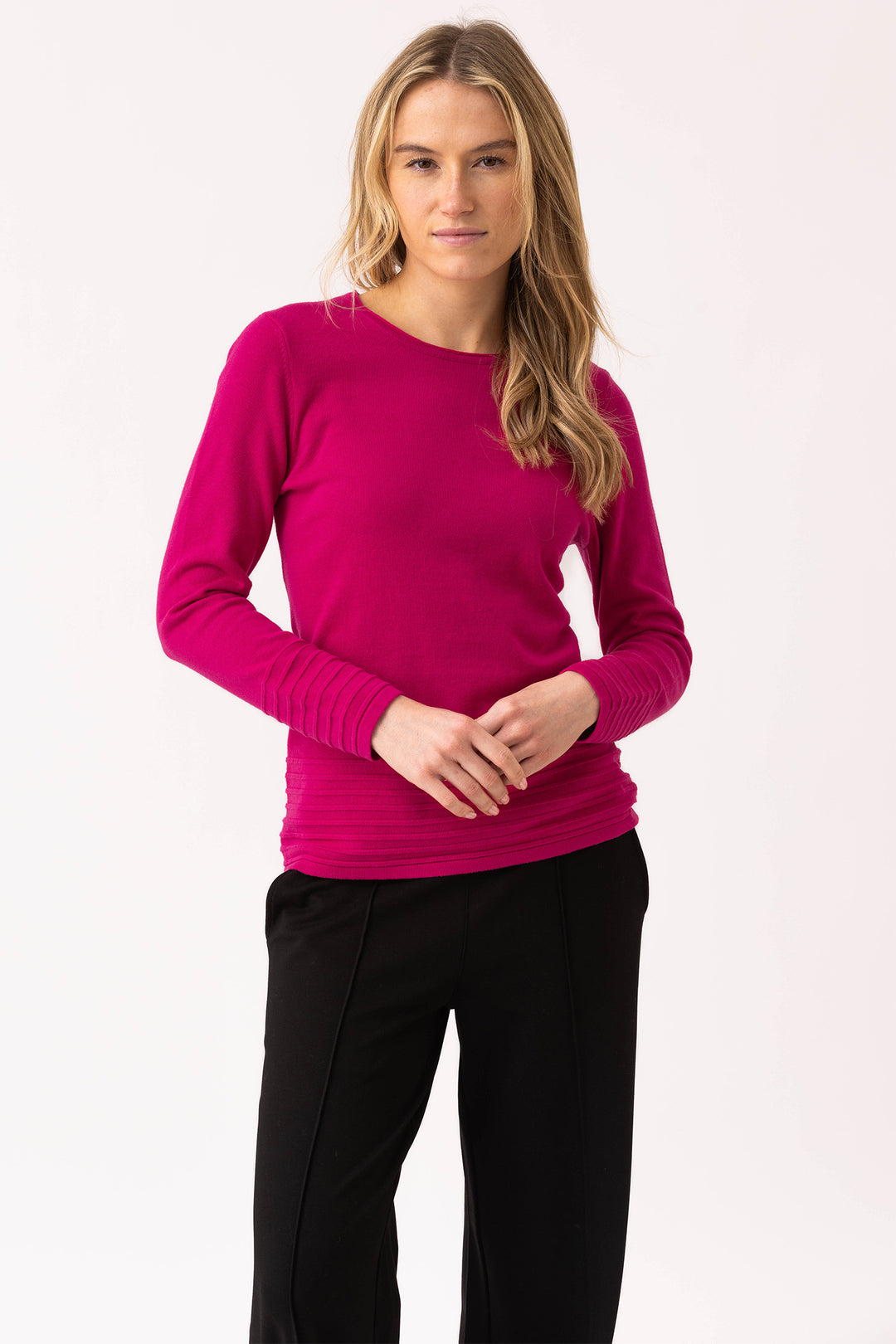 Woman wearing a bright pink sweater and black pants on a white background