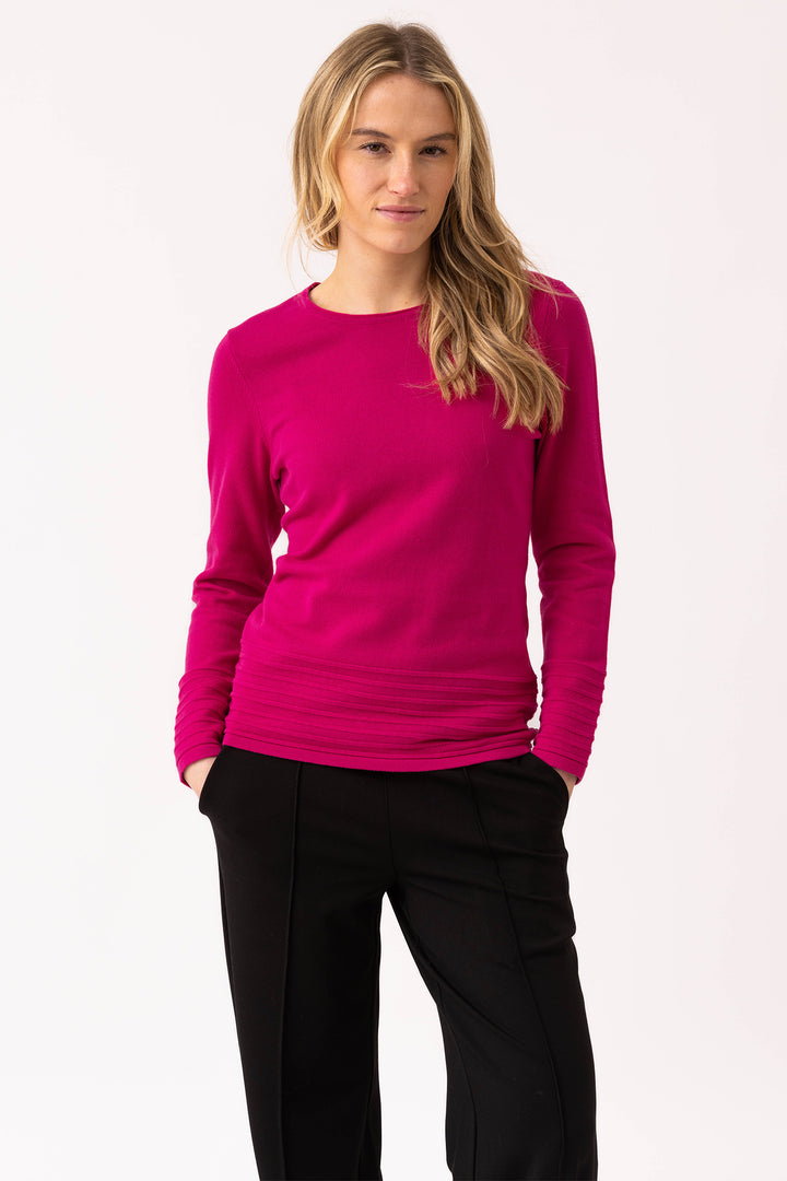 Woman wearing a bright pink long-sleeve top and black pants on a white background