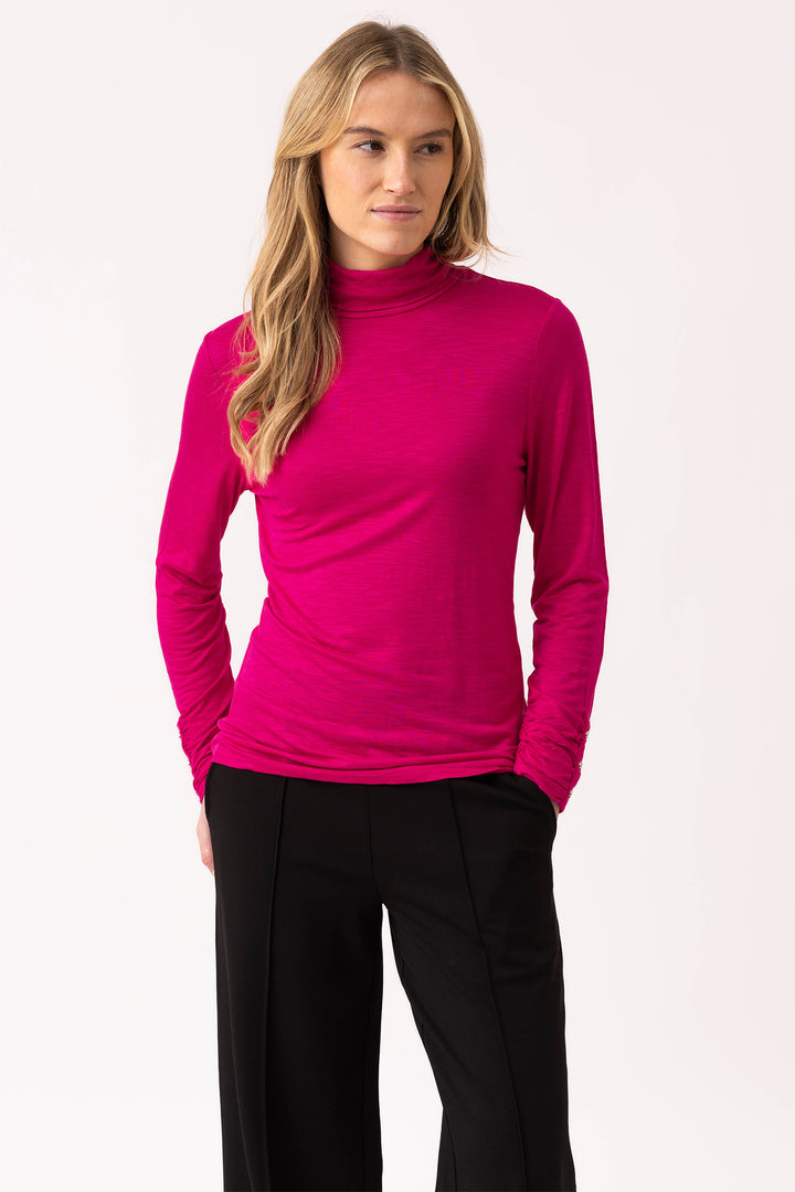 Woman wearing a bright pink long-sleeve top and black pants on a white background