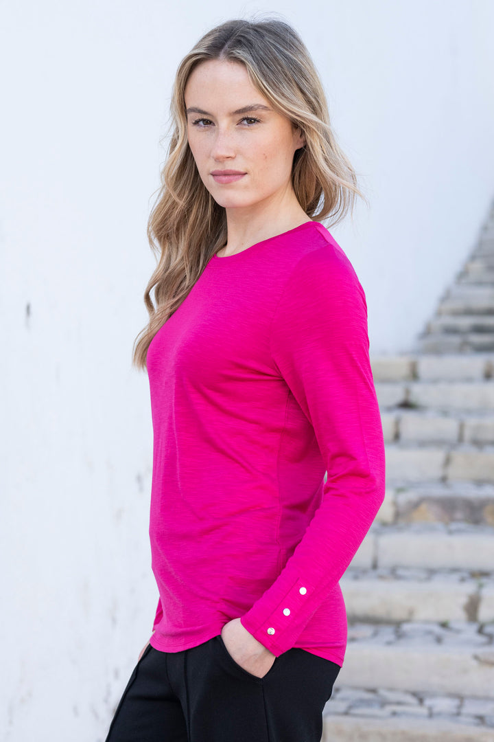 Woman wearing a bright pink long-sleeve top with a blurred outdoor background