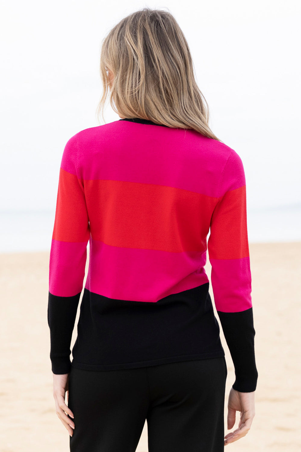 Person wearing a colorful striped sweater with a black base on a beach.