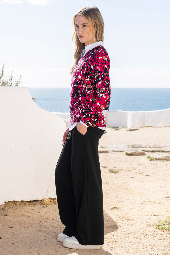 Woman wearing a colorful spot jumper and black pants standing on a beach.