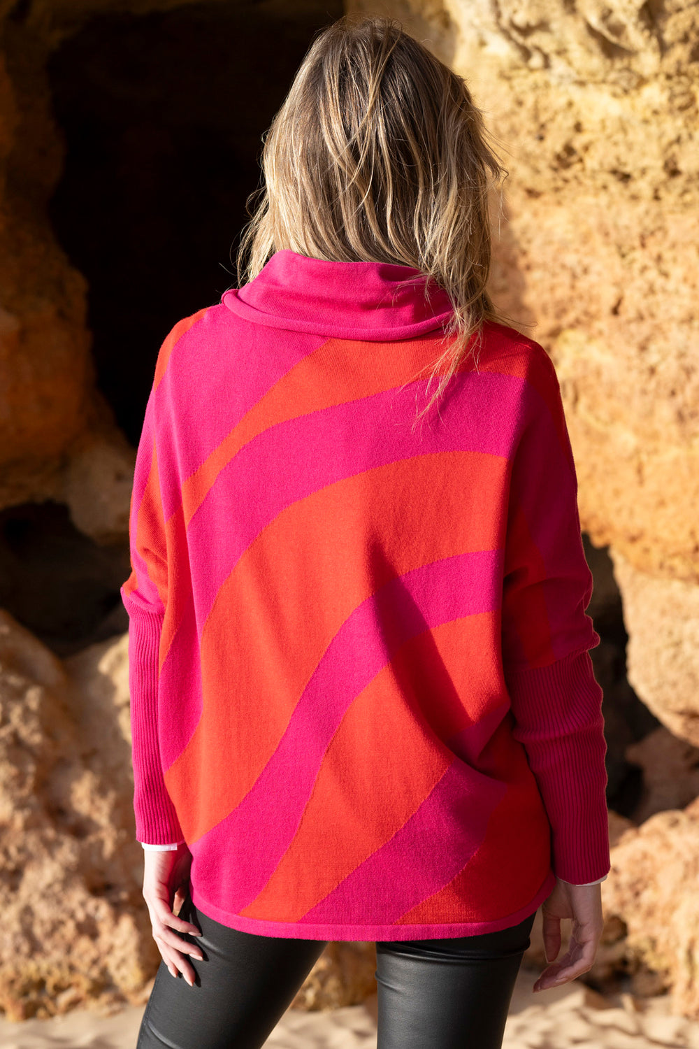 Person wearing a red and pink patterned sweater standing against a rocky background