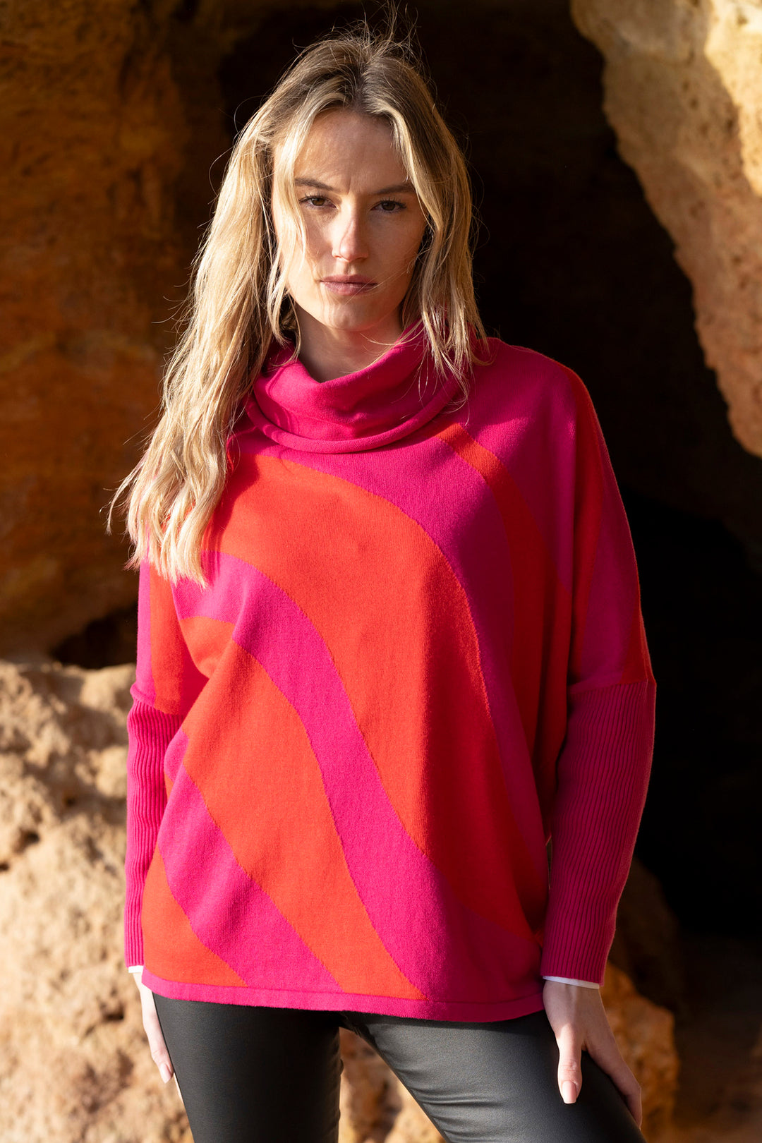 Woman wearing a bright pink and orange sweater in a natural setting.