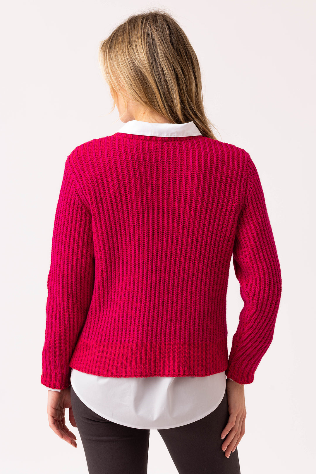 Person wearing a bright pink sweater over a white shirt on a plain background