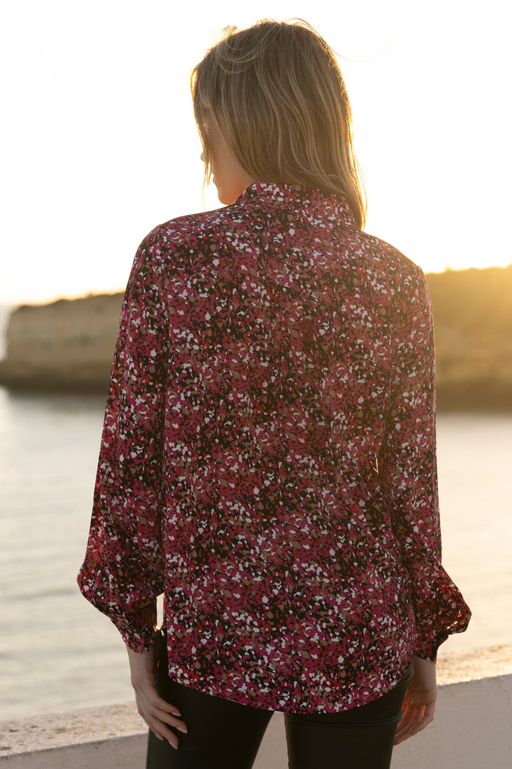 Person wearing a floral blouse by a body of water with a sunset.