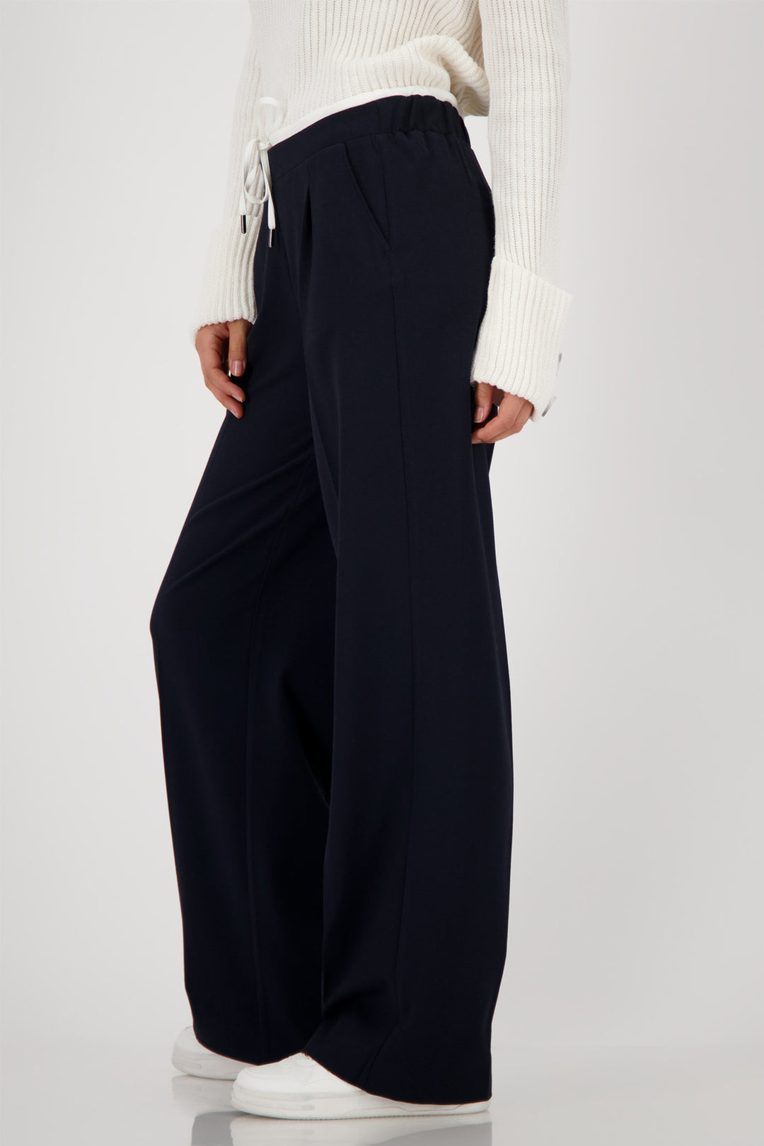Person wearing navy wide-leg pants with a white top on a light gray background
