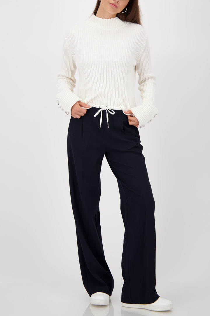Person wearing a white sweater and black pants on a white background