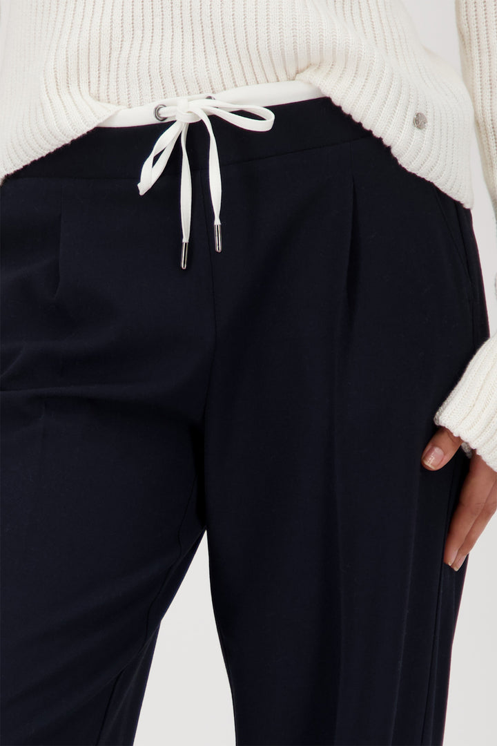 Black pants worn with a white sweater on a light background