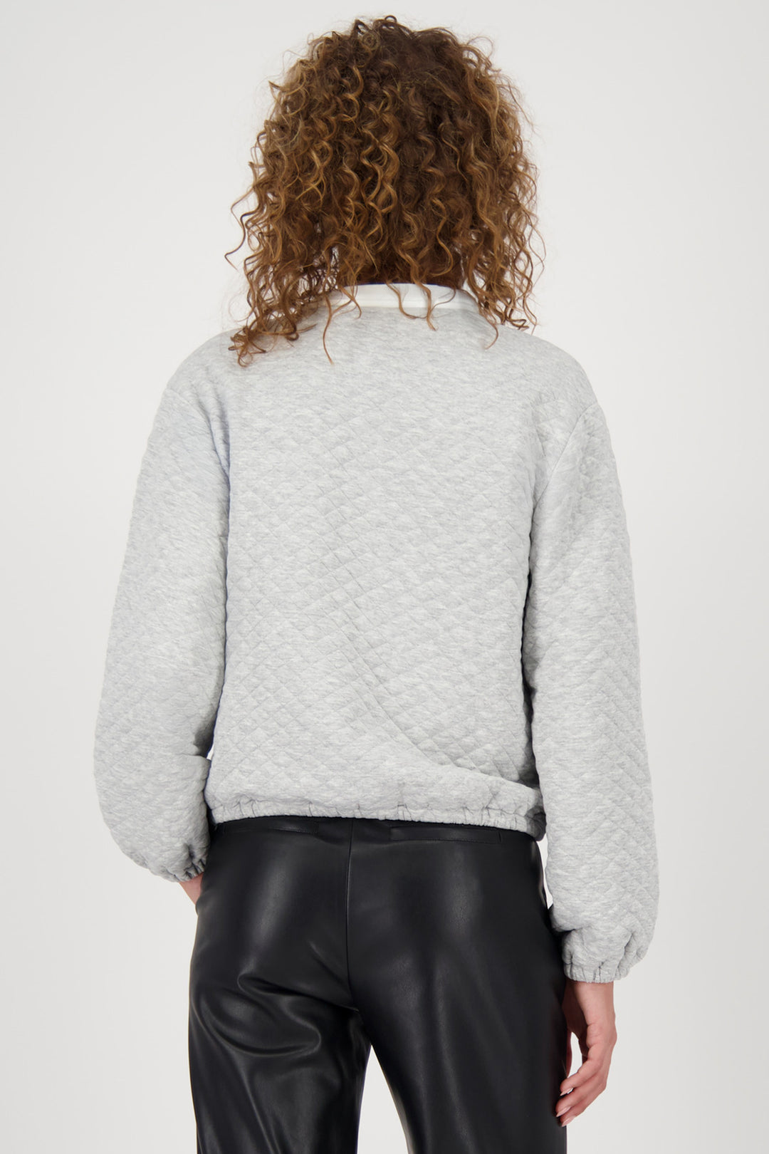 Person wearing a light gray textured sweater and black pants on a white background