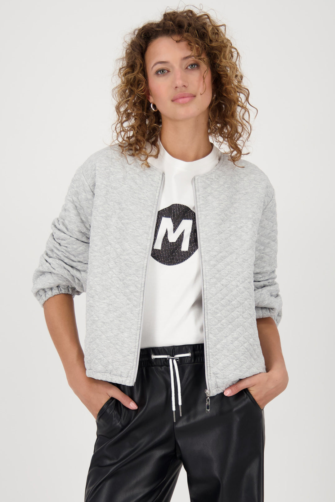 Woman wearing a gray jacket, white t-shirt with a black logo, and black pants on a white background