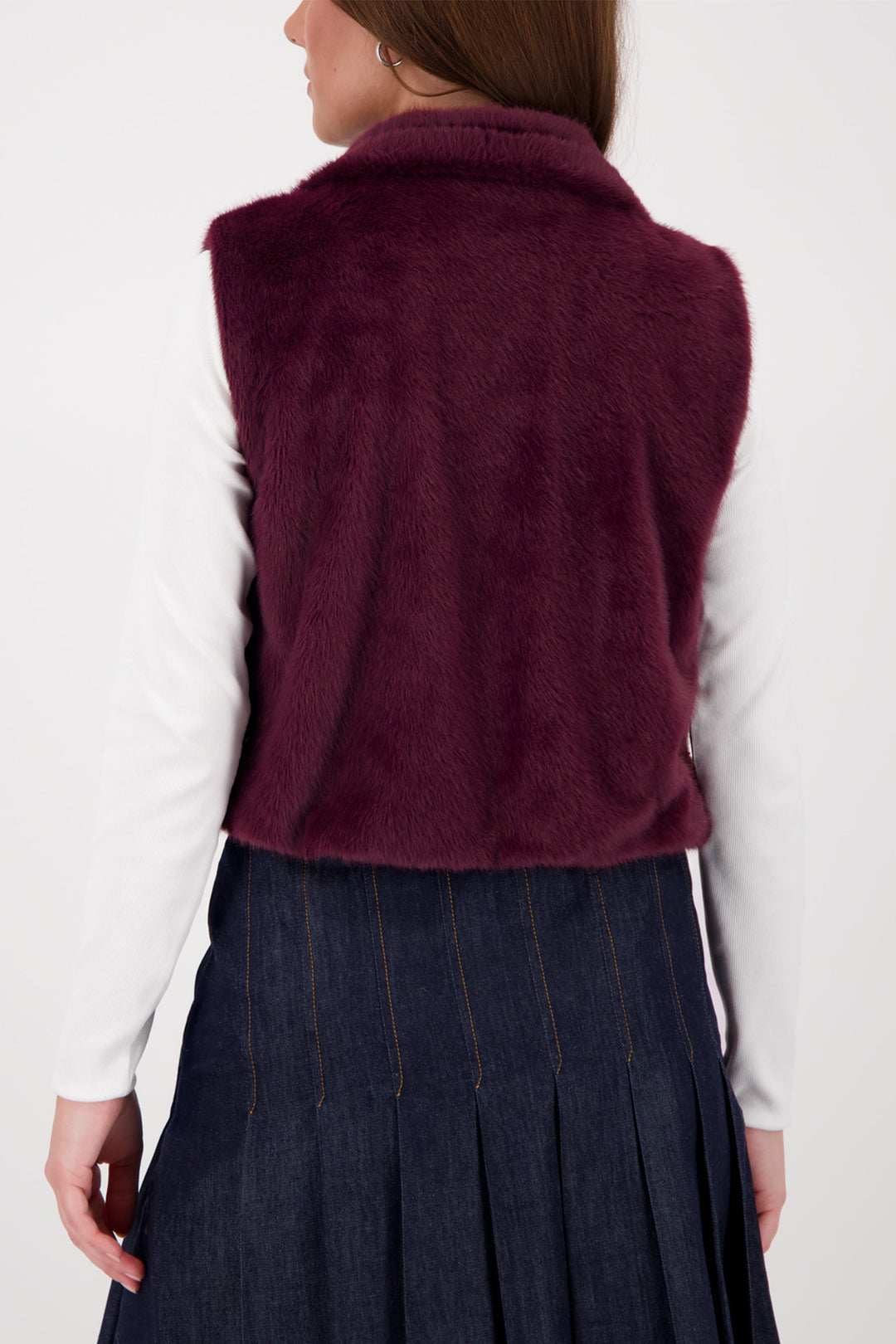 Person wearing a burgundy vest over a white shirt and dark blue skirt on a white background