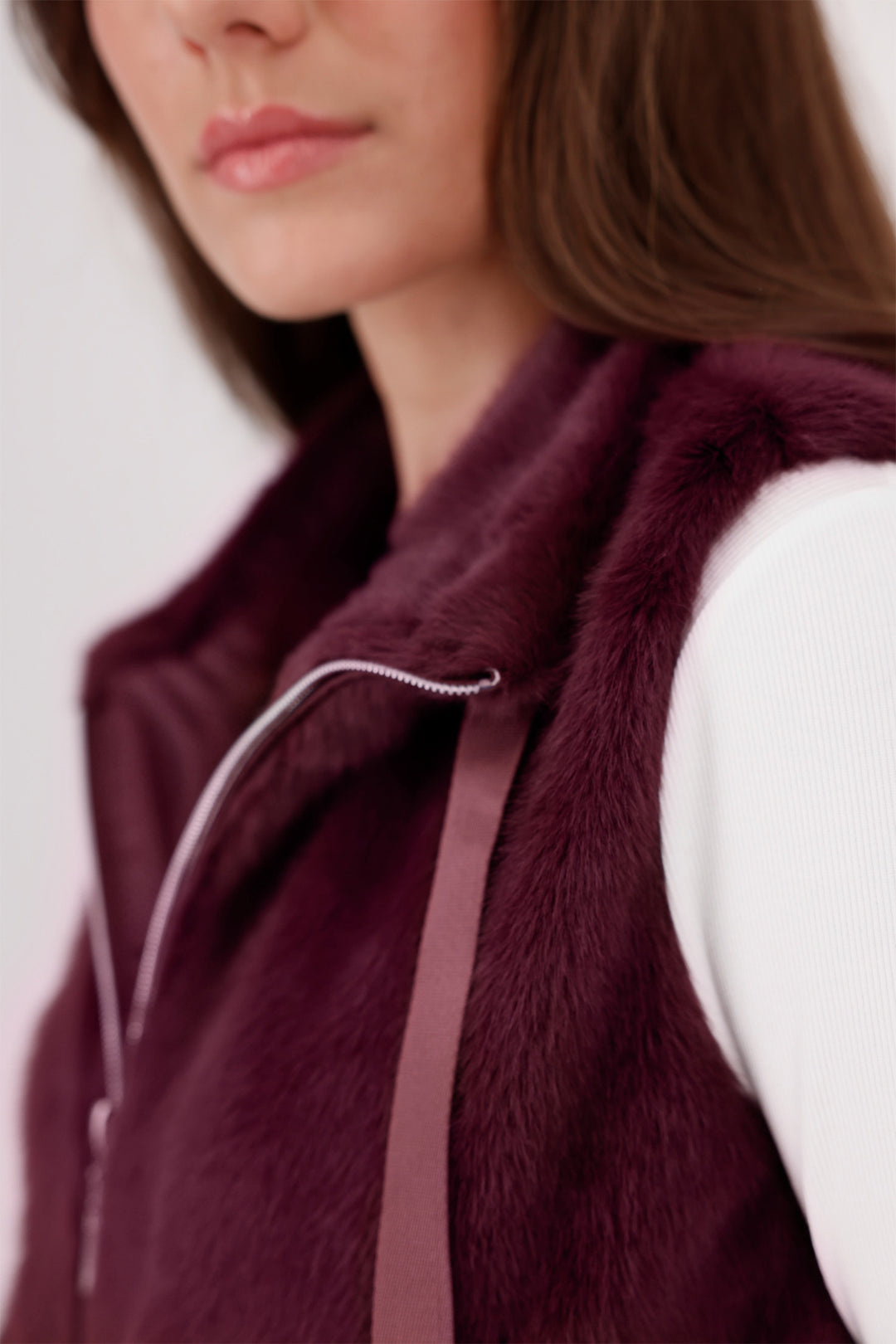 Close-up of a person wearing a burgundy fur vest with a blurred background