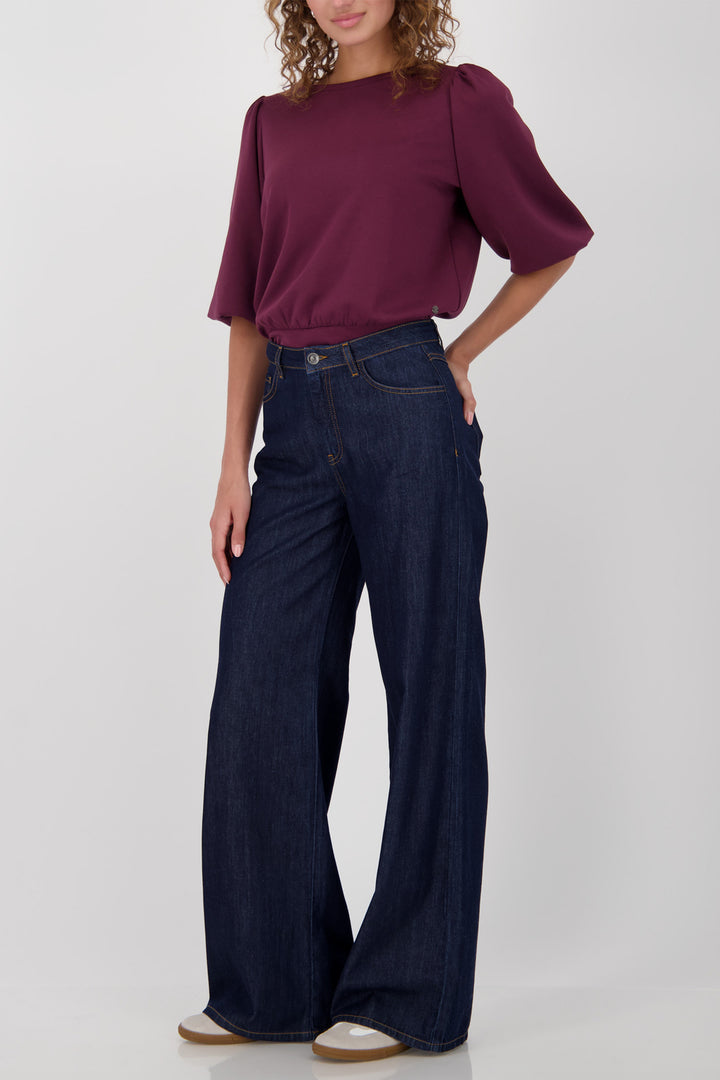 Woman wearing a burgundy top and blue jeans on a white background