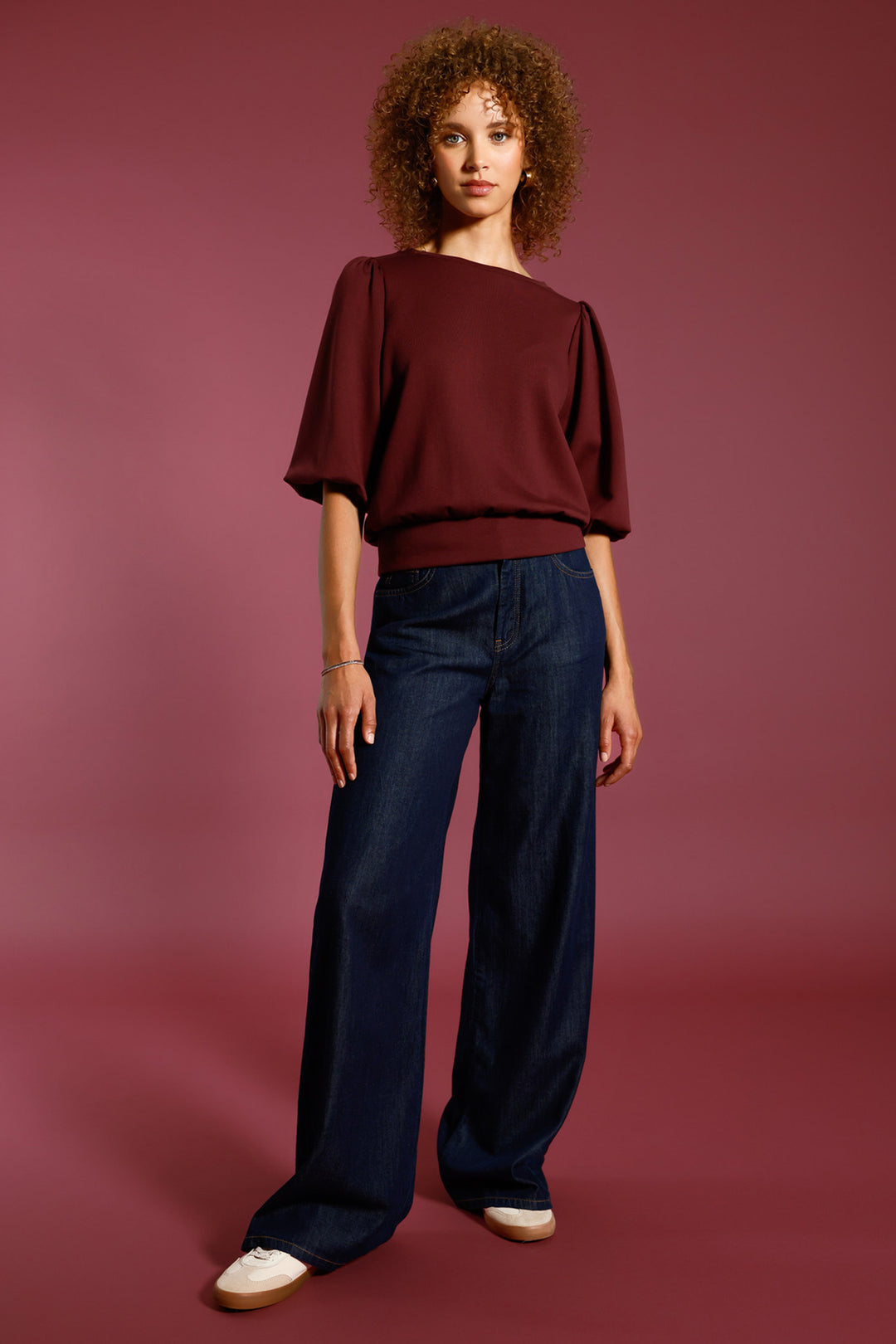 Woman wearing a burgundy top and blue jeans against a maroon background