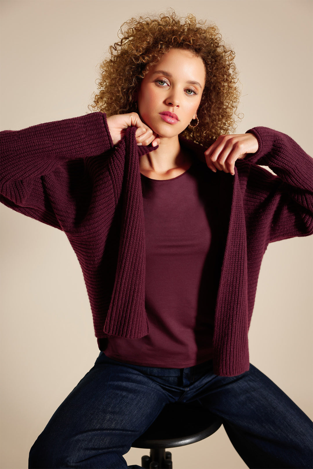 Woman wearing a maroon sweater over a plain shirt against a beige background