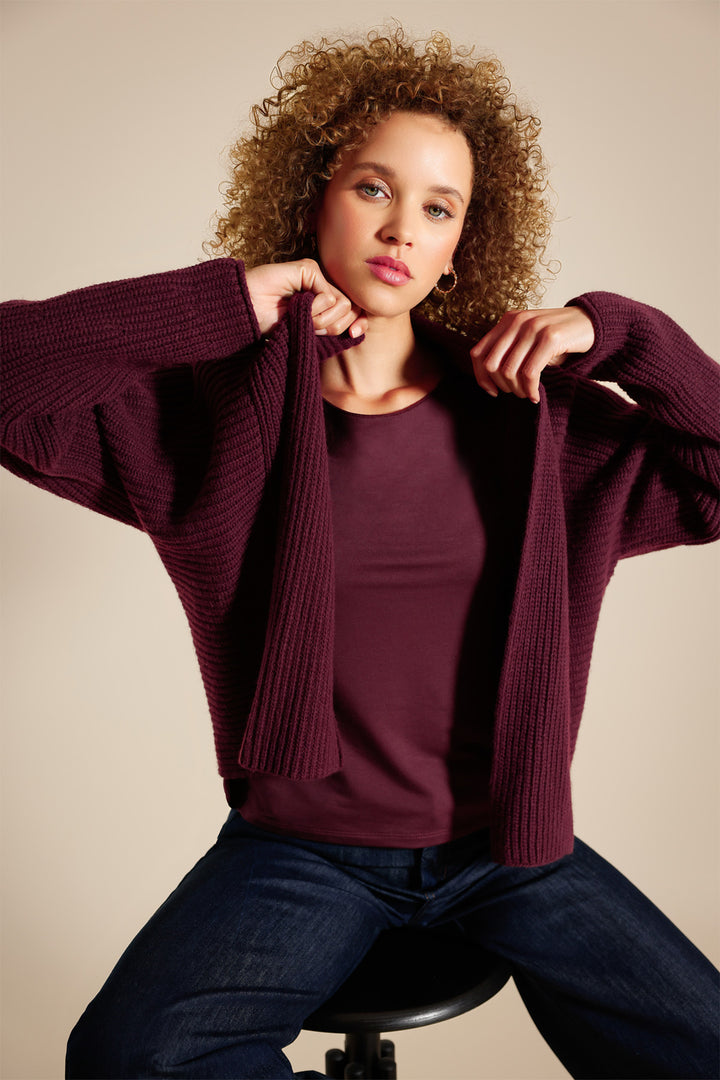 Woman wearing a maroon sweater over a plain shirt against a beige background