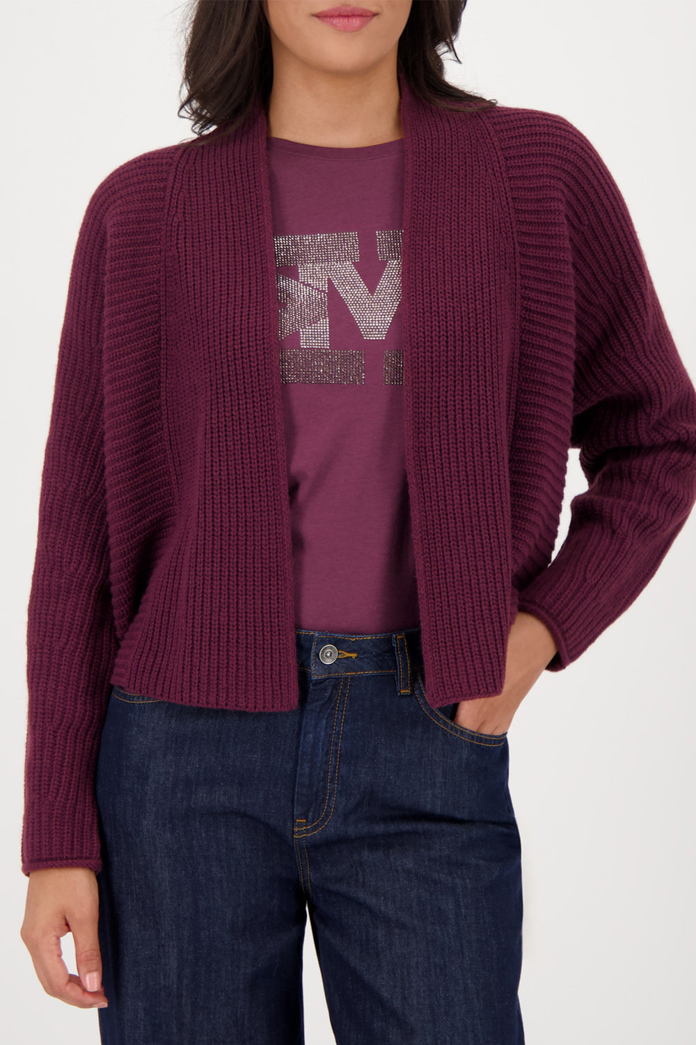 Person wearing a purple cardigan over a graphic t-shirt and blue jeans on a white background