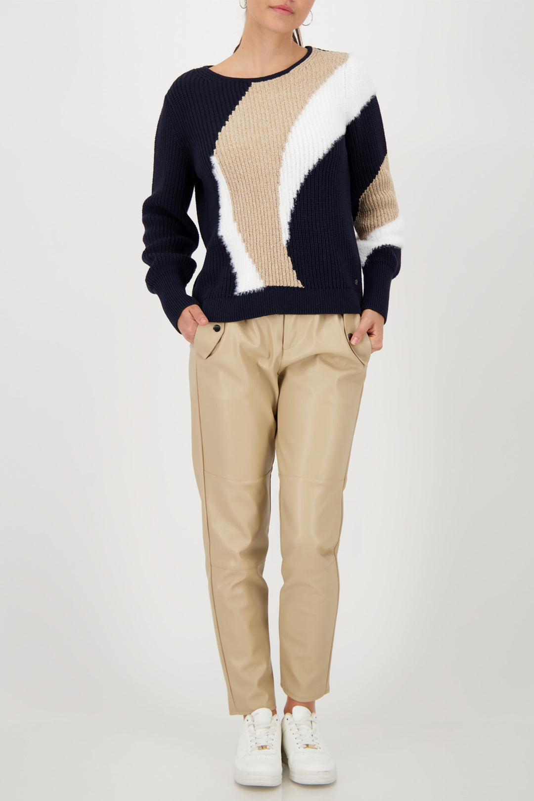 Person wearing a color-blocked sweater and beige pants on a white background