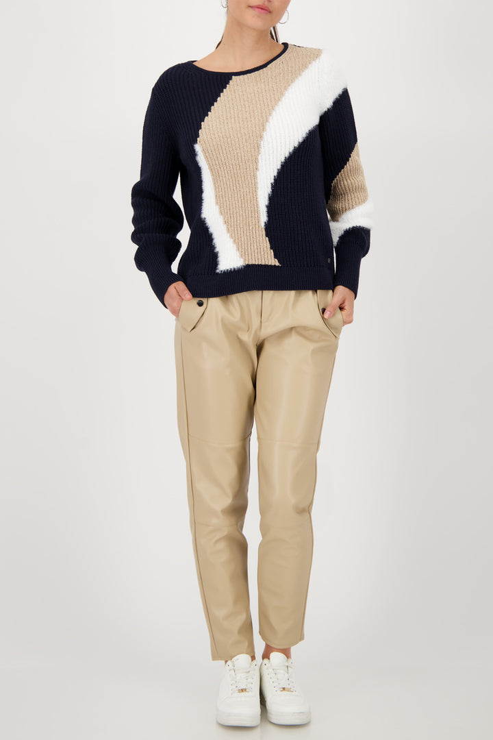 Person wearing a color-blocked sweater and beige pants on a white background