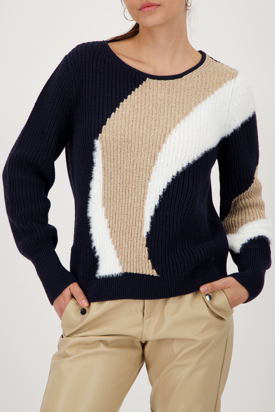 Person wearing a color-blocked sweater with navy, beige, and white sections on a plain background.